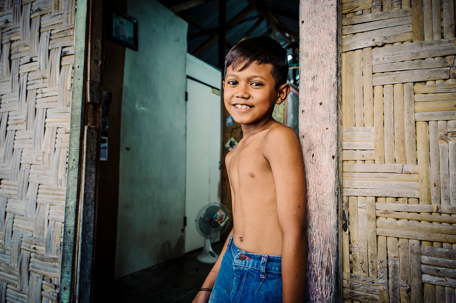 A young boy smiles at his home as he receives safe water.
